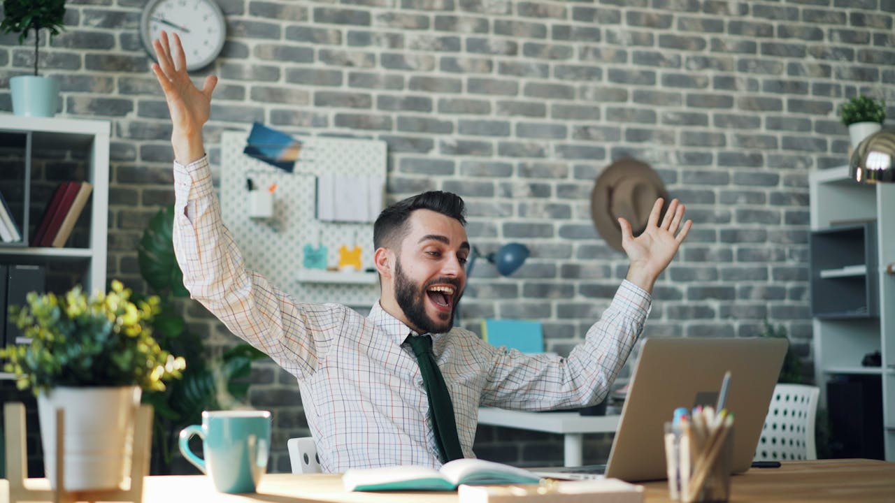 hero-img-01 A delighted office worker celebrating success at his desk in a modern office setting.